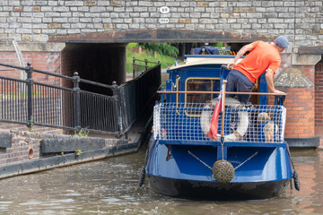 blue and cream canal boat being driven through small gap in tunnel under bridge in a tight fit