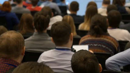 The journalism concept: press session indoors of large room. Many male and female persons sit in and listen the speaker who discussing about finance, investment, marketing and management strategy