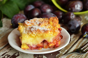 A square piece of cake with plums with crumble on a white plate