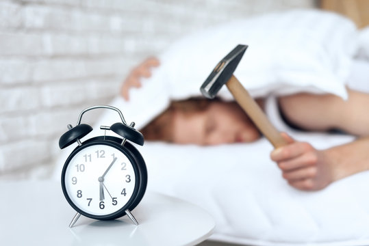 Young red haired man hammers alarm clock.