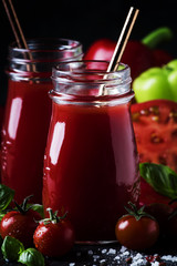 Spicy tomato juice with chili, bell peppers and green basil in glass bottles on black background, selective focus