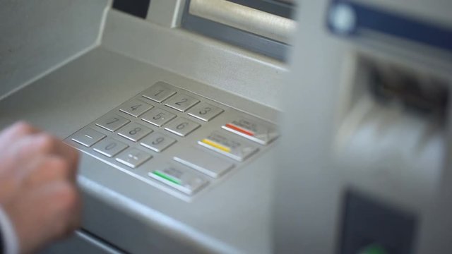 Businessman entering his pin code on keyboard of ATM, banking services, finance