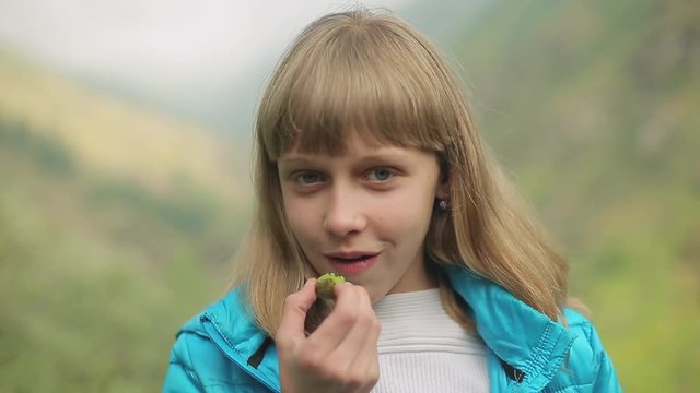 Portrait of a young beautiful woman, in the mountains in summer, eating sour green apricot