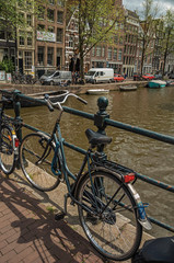 Bridge on canal with iron balustrade, bicycle, old buildings and boats in Amsterdam. Famous for its huge cultural activity and full of graceful canals. Northern Netherlands.