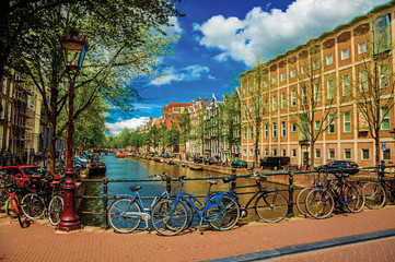 Fototapeta premium Bridge on canal with iron balustrade, old buildings and bicycles in Amsterdam. Famous for its huge cultural activity and full of graceful canals. Northern Netherlands. Retouched photo.