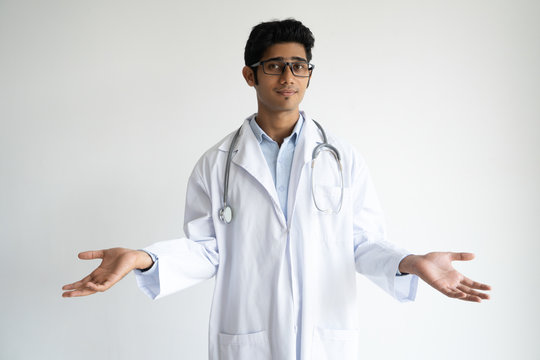 Confused Indian Doctor In Lab Coat Expressing Misunderstanding. Serious Indifferent Young Clinical Worker With Stethoscope On Neck Shrugging Shoulders And Looking At Camera. Puzzlement Concept