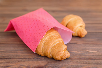 Two croissants in pink wrap on brown wooden table