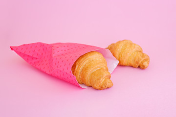 Two fesh croissants in pink paper wrap on pink background