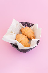Two croissants in basket on pink background