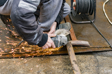 Industrial worker cutting a metal square pipe on a construction site with a manual electric grinder