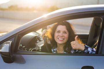 Happy woman showing thumb up and driving a new car