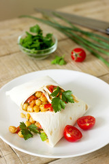 Burrito or shawurma with chickpeas, tomatoes and parsley on a light plate.