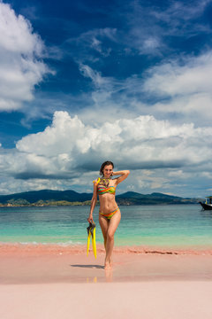 Beautiful young woman smiling while holding snorkeling equipment at Pink Beach during summer vacation in Komodo Island, Indonesia
