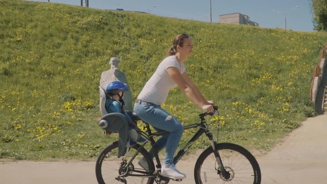 Happy mother with her little son are riding a bicycle in park. Slow motion