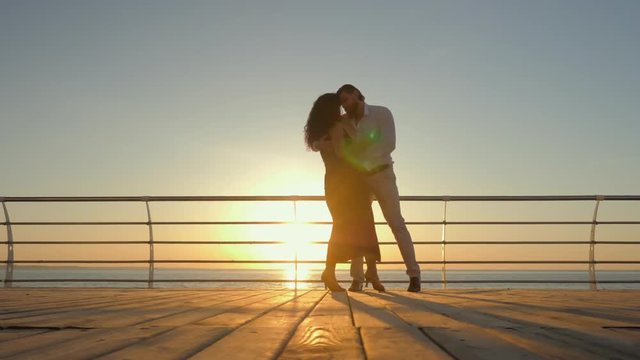 Energetic spanish couple against the background of the sunrise and ocean demonstrates elements of sensual Latin dance: bachata, rumba or kizomba. Slow motion.