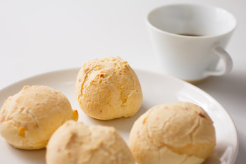Pao de Queijo is a cheese bread ball from Brazil. Also known as Chipa, Pandebono and Pan de Yuca. Snacks on white plate and cup of coffee.