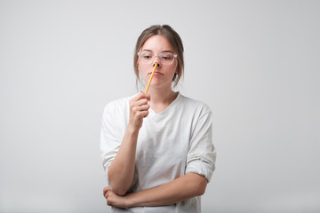 European girl in glasses thought with a pencil. She has no idea or plan what to do