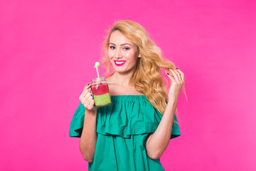Young beautiful woman with green smoothie on pink background