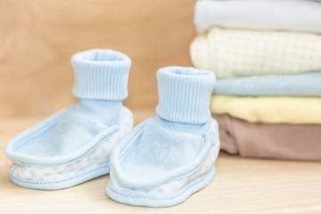 Obraz na płótnie Canvas Little blue shoes - booties and clothes on natural wooden background. Pastel clothes for baby infant. Newborn. Home cosiness.