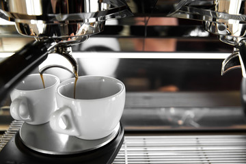 Italian espresso machine on a counter in a restaurant dispensing freshly brewed coffee into two small cups