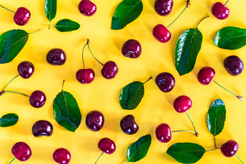 Sweet ripe cherries and leaves on yellow background