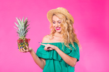 Happy young woman holding a pineapple on a pink background. Summer, diet and holidays concept