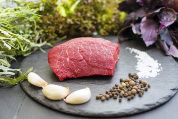 Raw beef on black board with spices, fresh rucola, lettuce, lollo-roso salad.