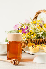 Jar of honey on a table with flowers, dessert and other ingredients
