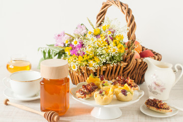 Jar of honey on a table with flowers, dessert and other ingredients