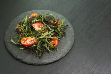 Healthy salad on stone table, arugula, tomatos, sesame seeds, olive oil Top view with copy space