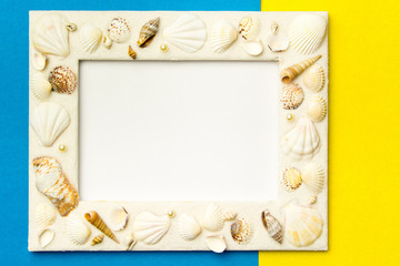 Photo frame with shells on blue and yellow color paper texture background. The concept of a summer vacation.  Summer Flatlay Image