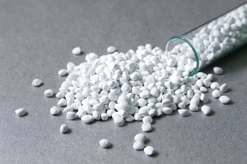 Fototapeta na wymiar Plastic pellets. White Colorant for plastics, in test-tube against a silvery metallic background. Plastic Raw material .