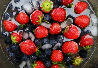 Obraz premium Strawberries and blueberries in a glass bowl with water and ice cubes