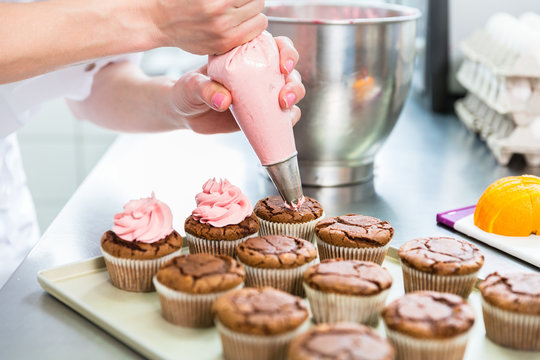 Frauen in Konditorei verzieren Cupcakes mit Spritzbeutel 