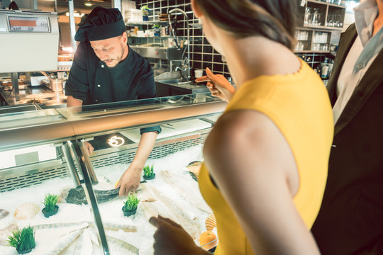 Koch zeigt den G&auml;sten seines Restaurants den empfehlenden frischen Fisch des Tages