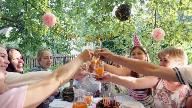 Family celebration or a garden party outside in the backyard. Steadicam shot. Happy family sit at a festive table and clink glasses