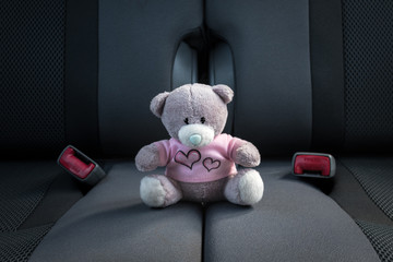 Small teddy bear sitting in a car without a safety belt. Child safety in a car concept.