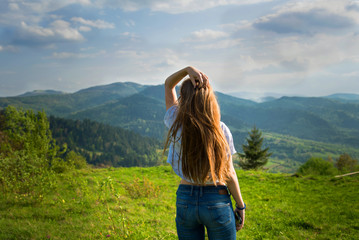Naklejka na ściany i meble Girl travel in mountains alone. Spring weather, calm scene. view over landscape in sunlight. Wanderlust photo series. View from the back. The Carpathians mountains.