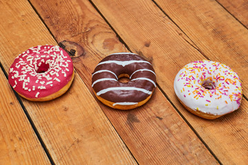 Three colorful appetizing donuts lie on wooden boards background.
