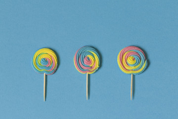 Creative view of colorful, handmade swirl lollipop in summer colors on blue paper background....