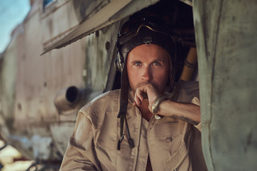 Portrait of a mechanic in uniform and flying near, standing under an old bomber airplane in the open air museum.