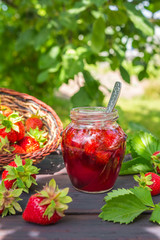 Strawberry jam and juicy ripe strawberries on a wooden table in the garden on a summer sunny afternoon in a rustic style, the concept of gardening, healthy organic vitamin nutrition