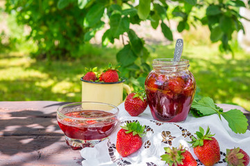 Strawberry jam and juicy ripe strawberries on a wooden table in the garden on a summer sunny afternoon in a rustic style, the concept of gardening, healthy organic vitamin nutrition