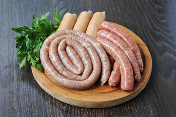 Assorted raw sausages on a round wooden board. Sausages of pork, beef and chicken. Dark background. Close-up.