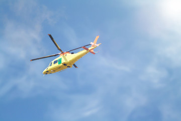 Yellow helicopter flying low above the ground against the sky
