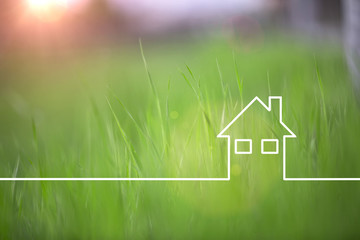 With a line drawn green eco house icon on sunny blurred grass copy space background. Selective focus used.