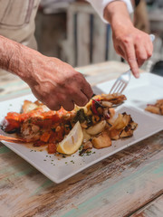 Manos de hombre, cocinero, cortando y repartiendo pescado en los platos de los comensales