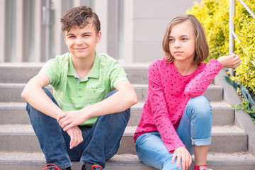 Happy teenage boy and girl smiling while sitting on the stairs outdoors. Young sister and brother teens.