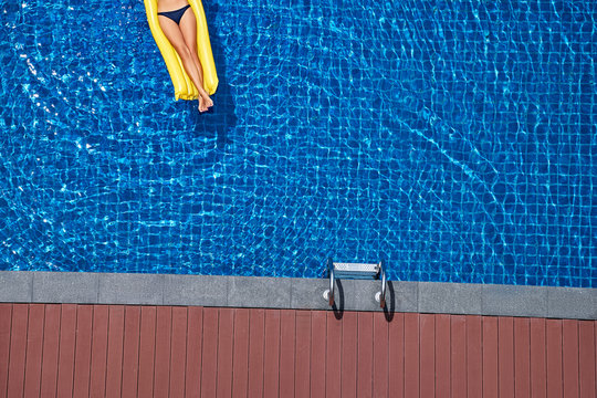 Enjoying suntan. Vacation concept. Top view of slim young woman on the yellow air mattress in the big swimming pool.
