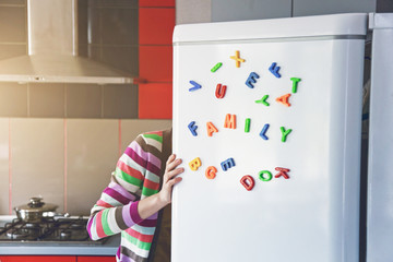 Woman looking in open fridge with Family letters on door. Cooking for children and husband concept